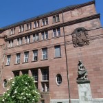 Kollegiengebäude I bears witness to a multi-layered history with a WWI memorial in front, university seal above, and now-removed swastika at the top, a dark history marked by absence.